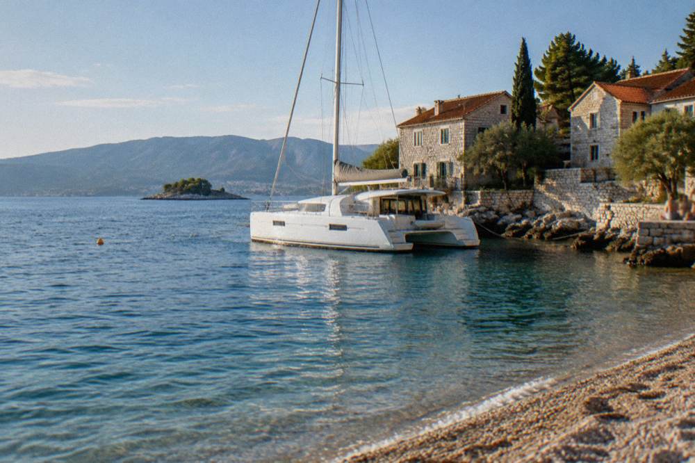 A white catamaran moored at a small island waterfront with stone houses