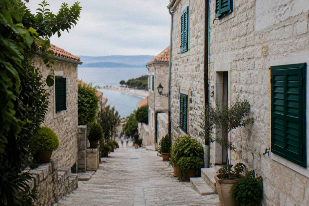 A quiet island street of pale stone houses with green shutters and potted plants