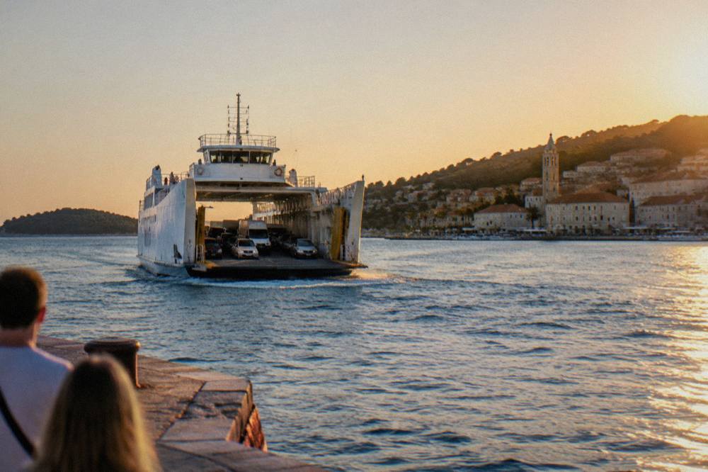 A large car ferry approaching an island port with vehicles visible on its open deck