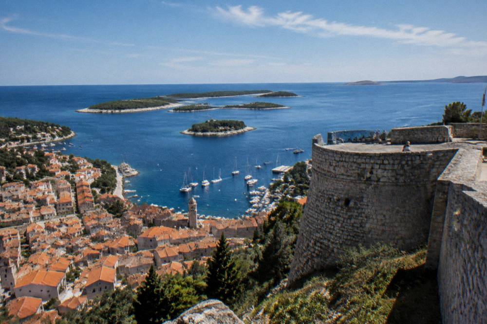 A hilltop fortress overlooking a red-roofed island town and a channel dotted with small islets