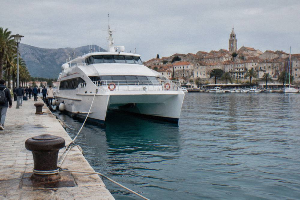 A white fast catamaran moored at a busy Adriatic ferry port in the morning