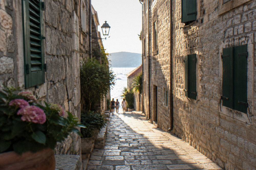 Narrow stone lane in an old Dalmatian town with shuttered houses and sunlight at the far end