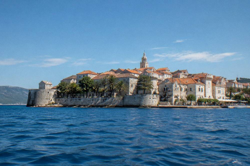 A walled seaside town seen from the water under a clear summer sky
