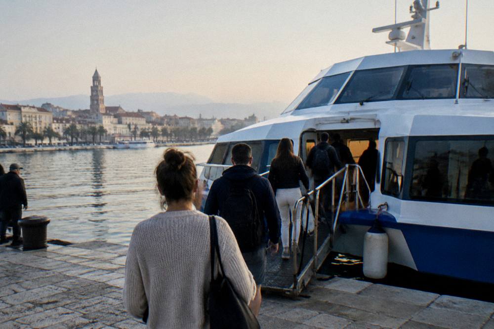 Passengers boarding a fast passenger boat at a city waterfront in early morning light
