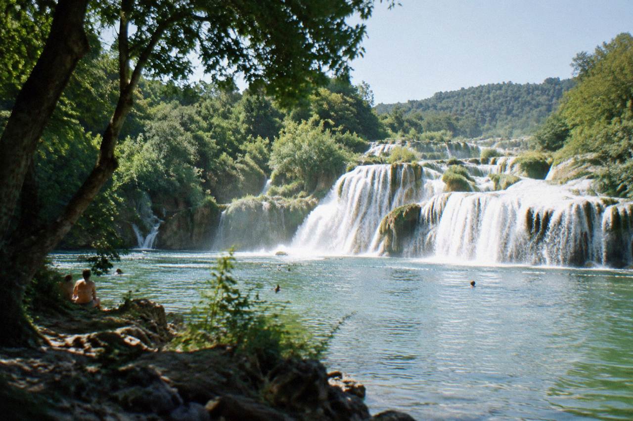 Wide waterfalls cascading over limestone steps into a green river pool