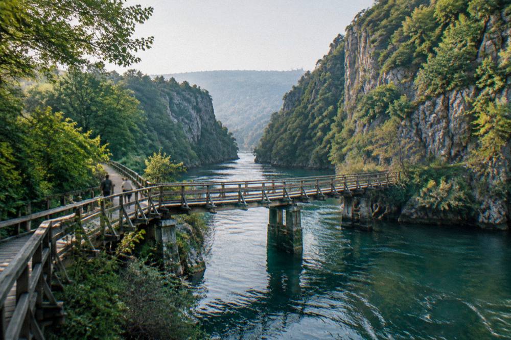 Wooden footbridge crossing a narrow river gorge with steep green cliffs
