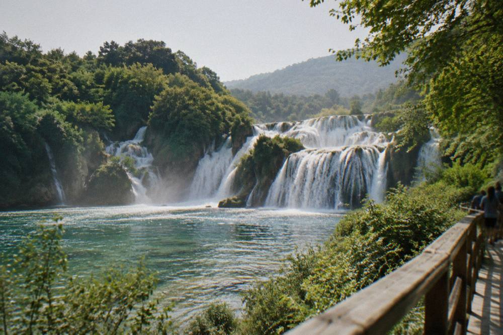 Waterfalls in full flow surrounded by dense summer greenery