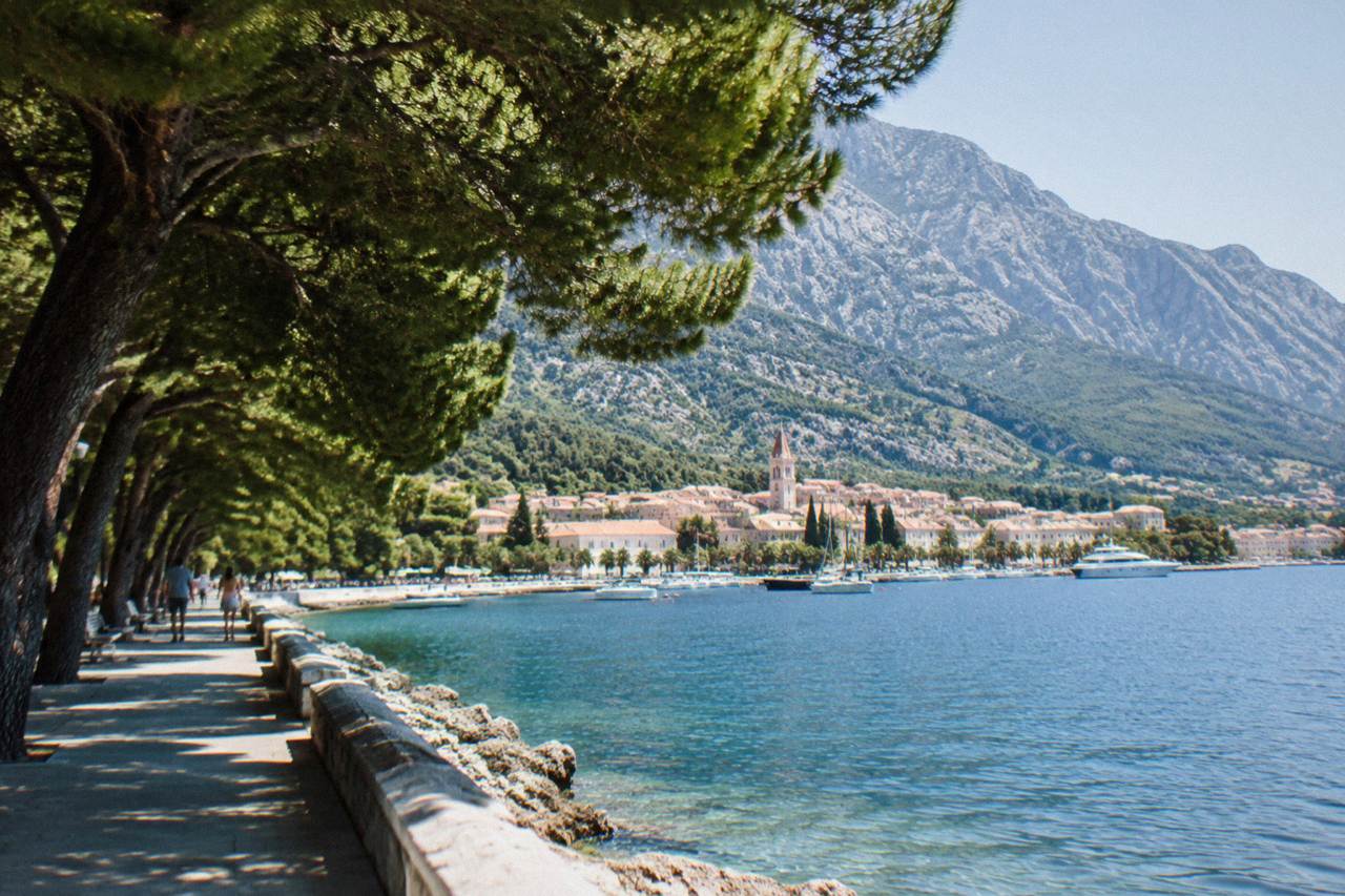 A seaside town on the Adriatic coast with a long promenade, pine trees and a mountain rising directly behind the rooftops