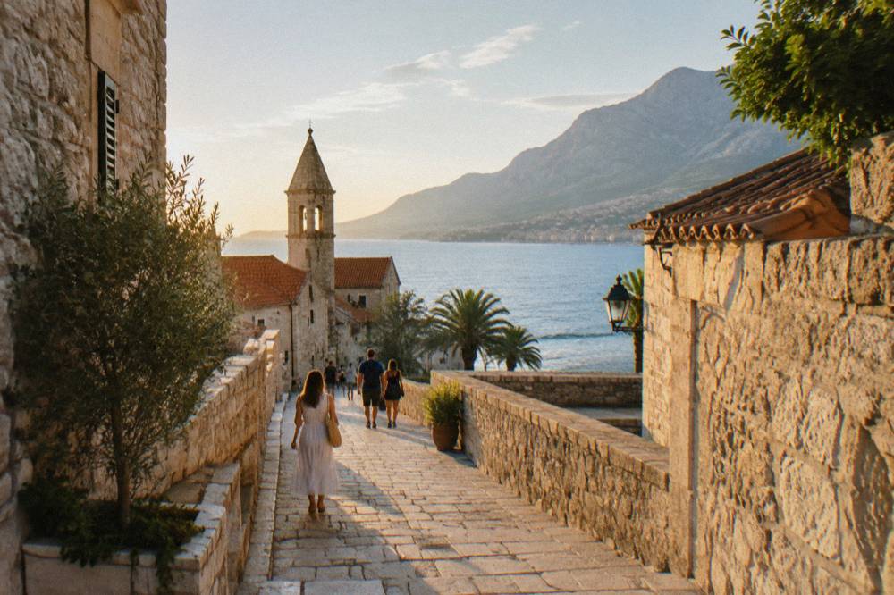 Tourists walking on pale stone streets of a small walled old town near the sea in bright morning light