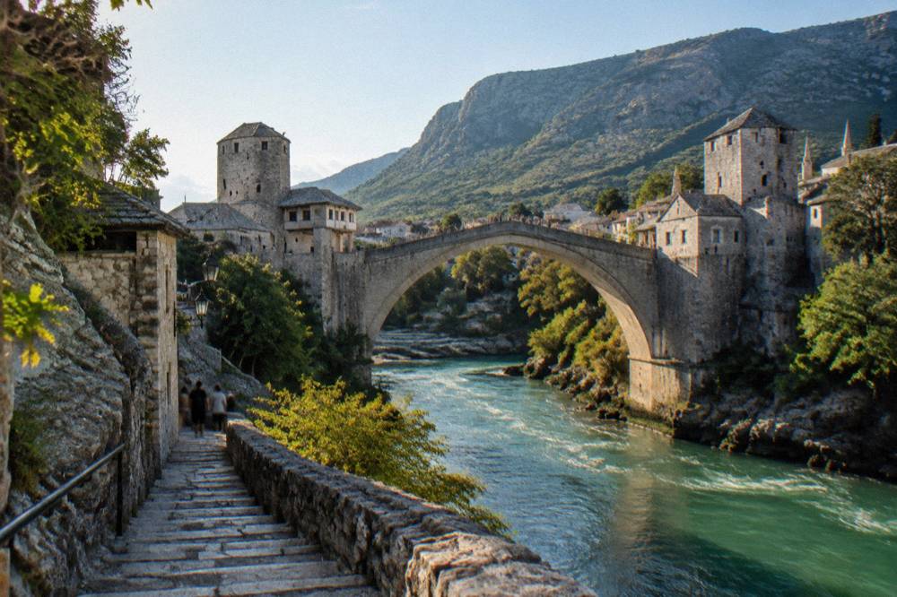 Bridge towers and steep stone steps beside a fast green river in a mountain valley