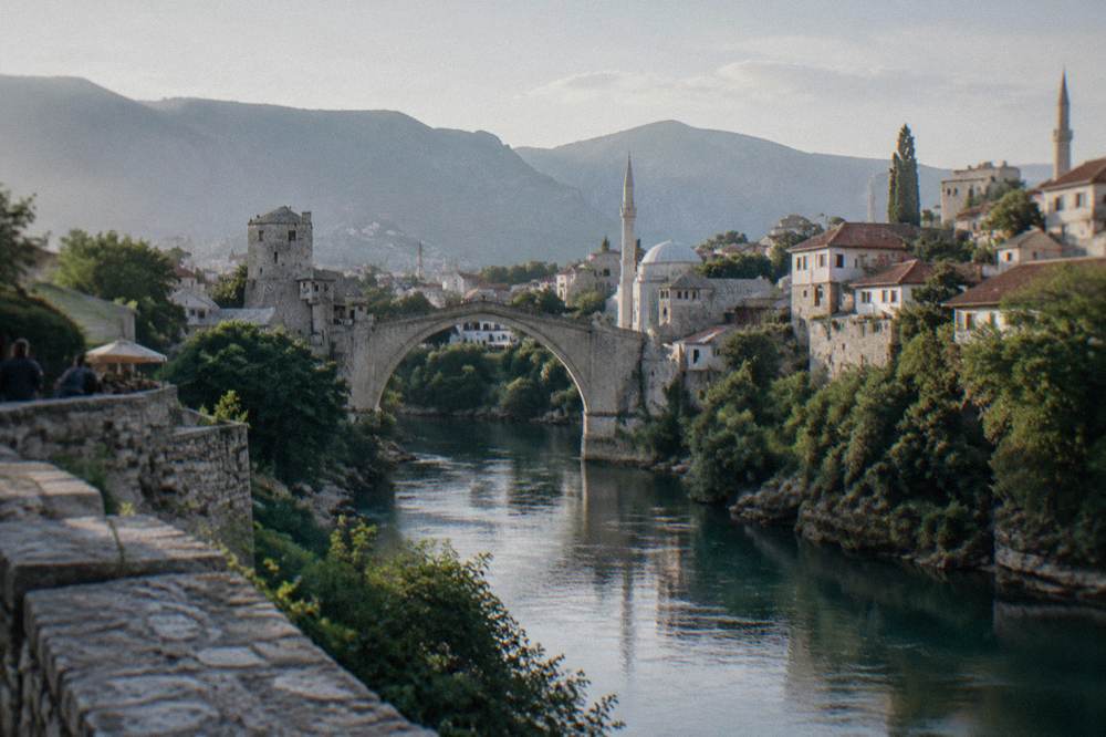 River panorama with a stone bridge, minarets and red roofs under hills