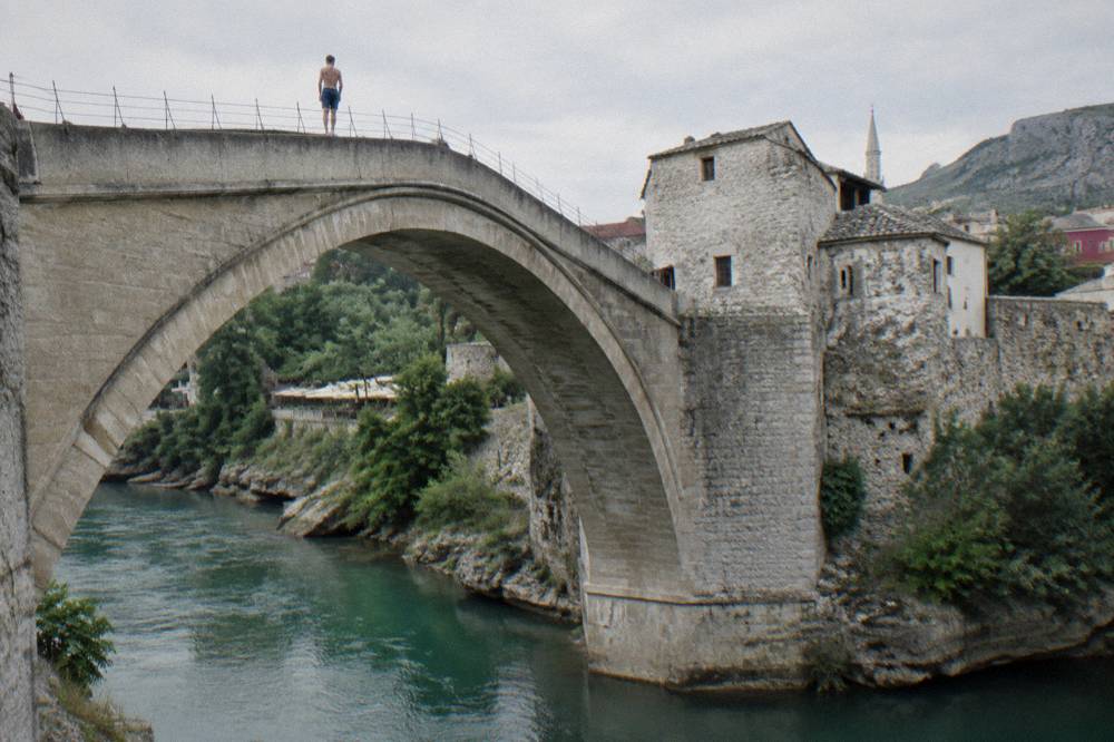 Diver standing on the top of a stone bridge arch above a green river