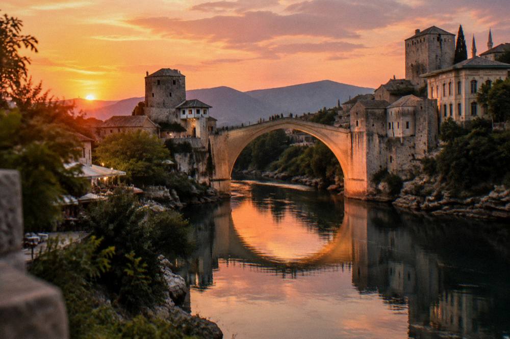 Sunlit stone bridge reflected in calm river water at dusk