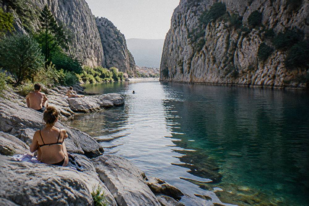 People in swimwear resting on smooth rocks beside a clear river in a narrow gorge