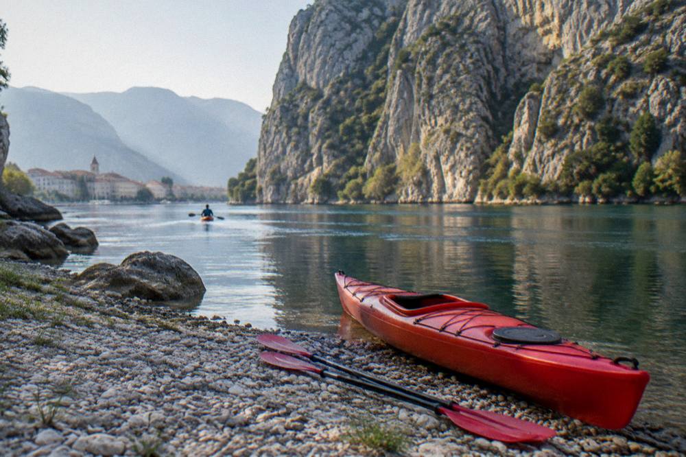 A red kayak and paddles resting on a stony riverbank with a canyon wall behind