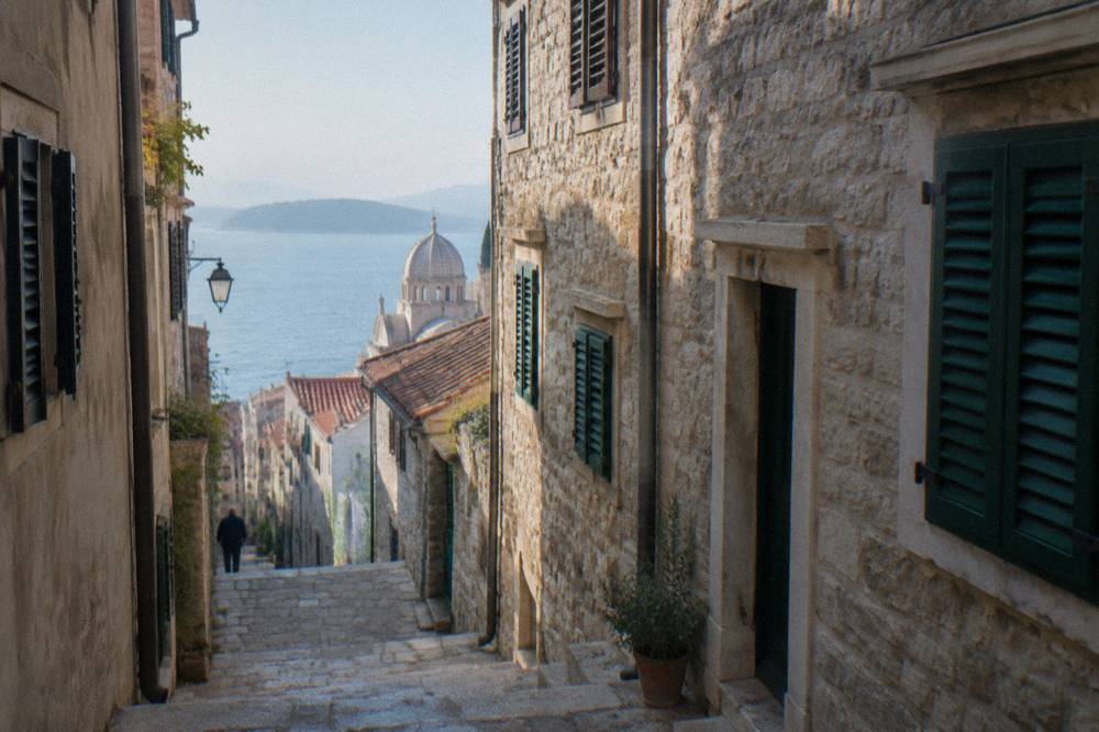 Narrow stone street in an old Dalmatian town with shutters and a glimpse of blue sea