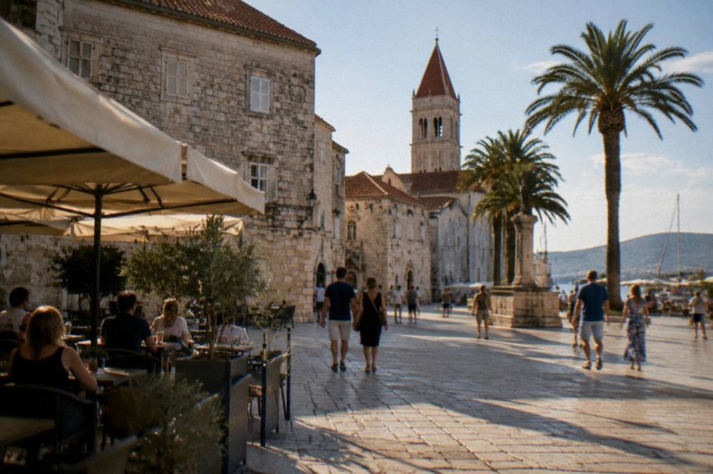 Sunny stone square with cafe tables and people strolling