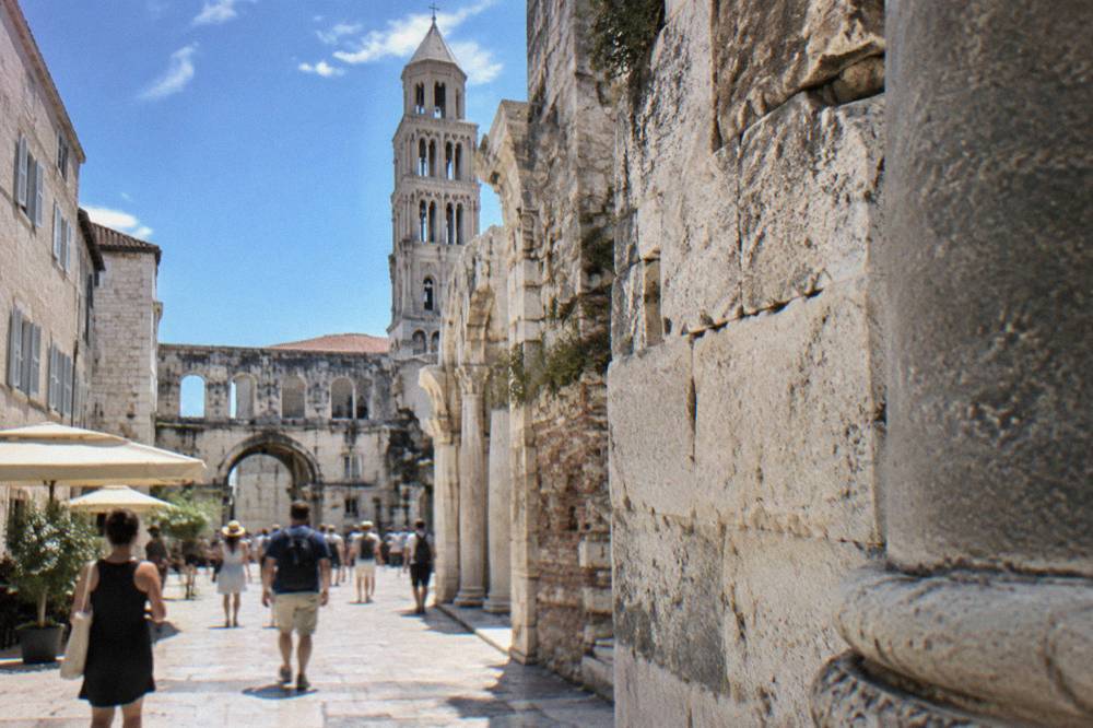 Tourists walking past Roman walls and stone buildings inside Diocletian's Palace old town