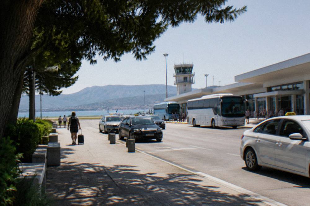 The departures forecourt of a small coastal airport with taxis and buses waiting in daylight