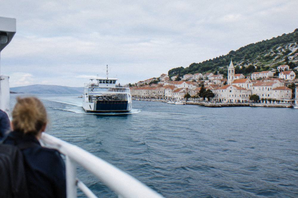 A car ferry approaching a island port town with white stone houses in the background
