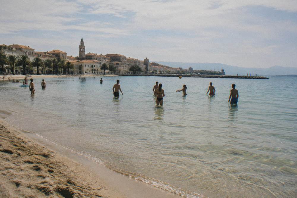 A sandy city beach with shallow clear water and people playing a ball game in the shallows