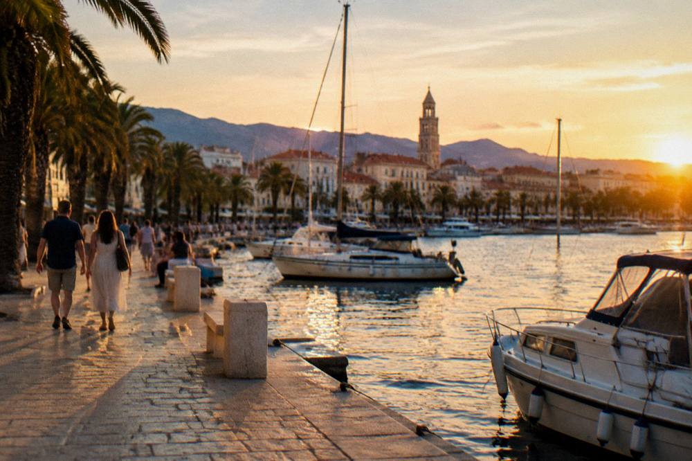 People strolling along the Riva promenade in Split at golden hour with palm trees and moored boats