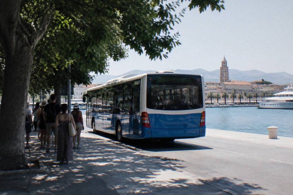 A city bus parked at a stop near Split harbour with passengers waiting in the shade