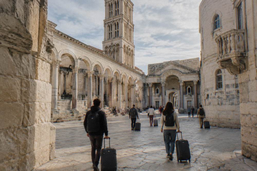 Travellers with suitcases walking across the stone-paved square in front of Diocletian's Palace