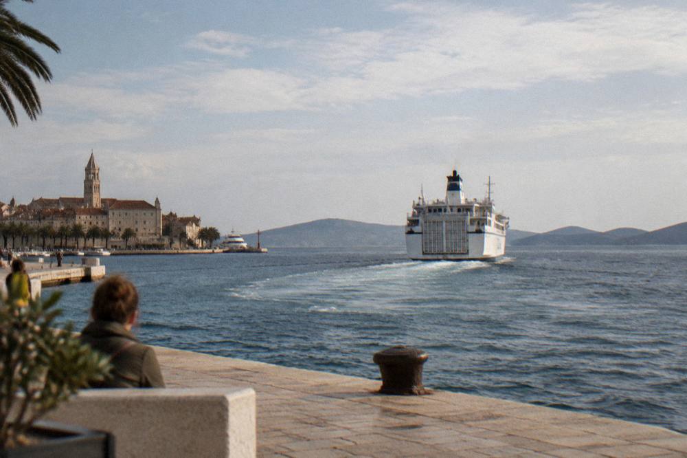 A white ferry pulling away from Split harbour with islands on the horizon