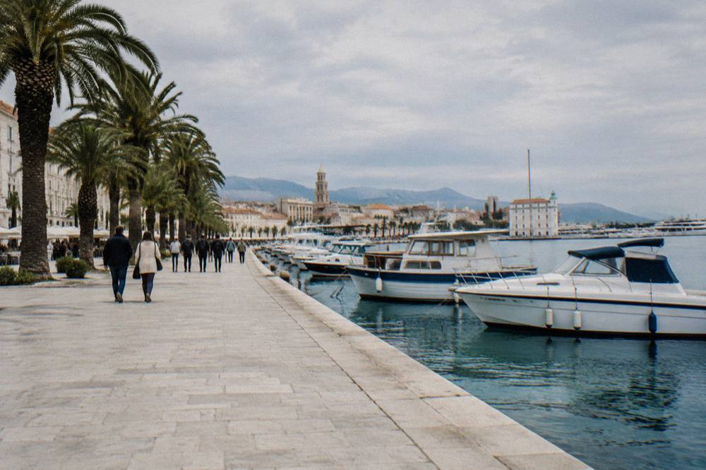 People strolling along the palm-lined Riva promenade in Split beside moored boats
