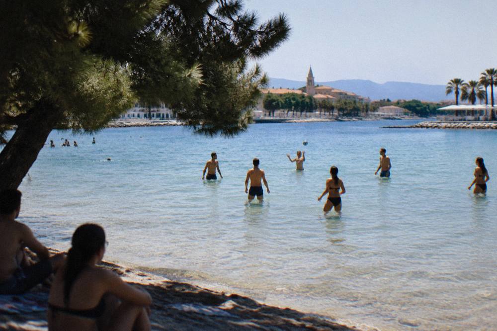 Shallow sandy shallows at a city bay with people standing in knee-deep clear water playing a ball game