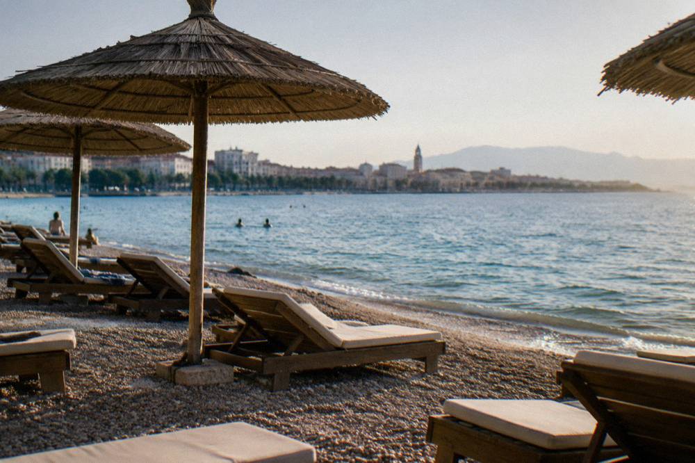 Sun loungers and umbrellas on a pebble shore in late afternoon light with calm turquoise water