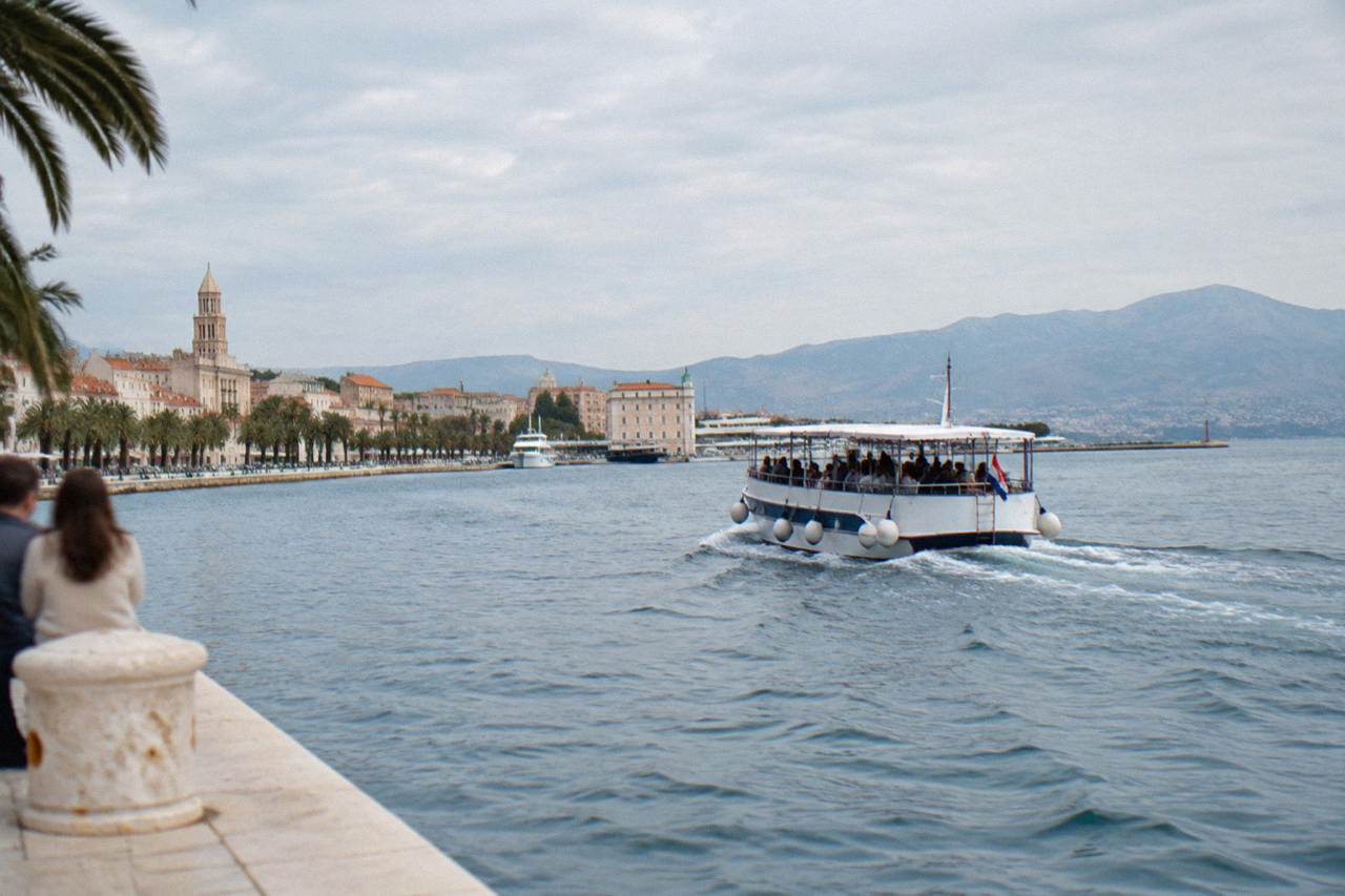 A motor boat full of passengers cruising away from the Split waterfront on a bright afternoon