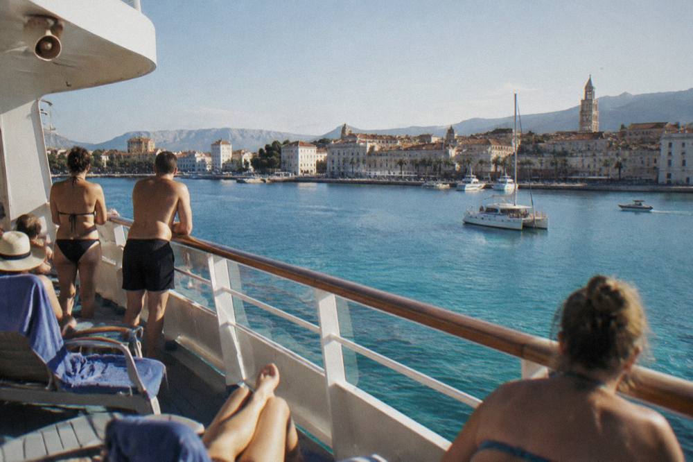 Passengers in swimwear on the deck of a cruise boat anchored in a turquoise cove