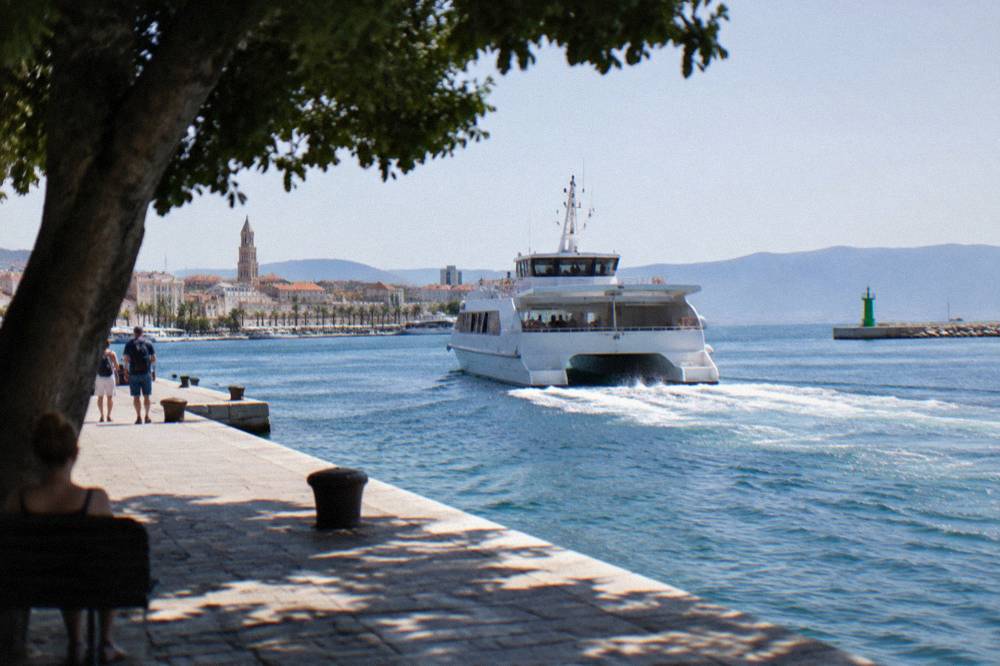 A white catamaran pulling away from a ferry berth in Split harbour in morning light