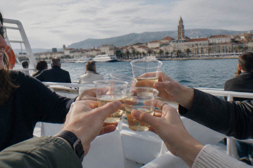 Friends clinking plastic cups of wine on the sun deck of a boat near Split