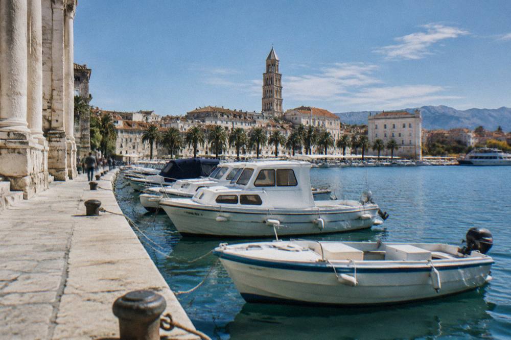Row of motorboats tied along a stone quay in Split harbour with the bell tower of the old town in the distance