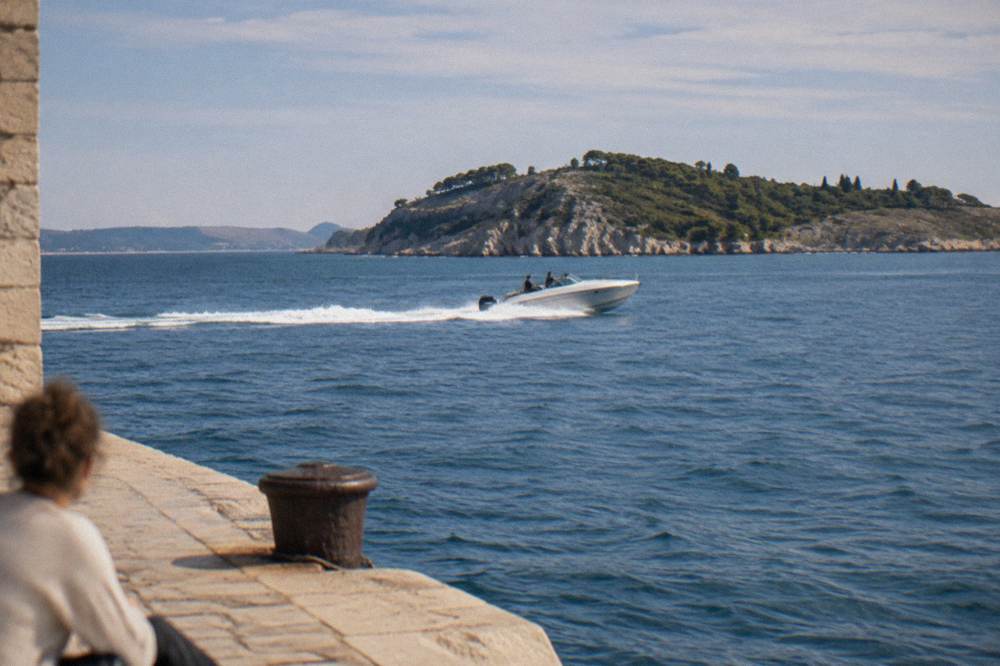 Speedboat cutting across open blue water towards a rocky island coastline