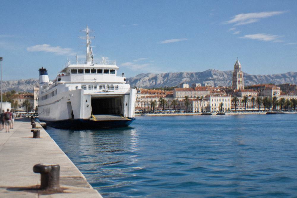 White ferry moored at a concrete pier in Split with the old town roofline behind it
