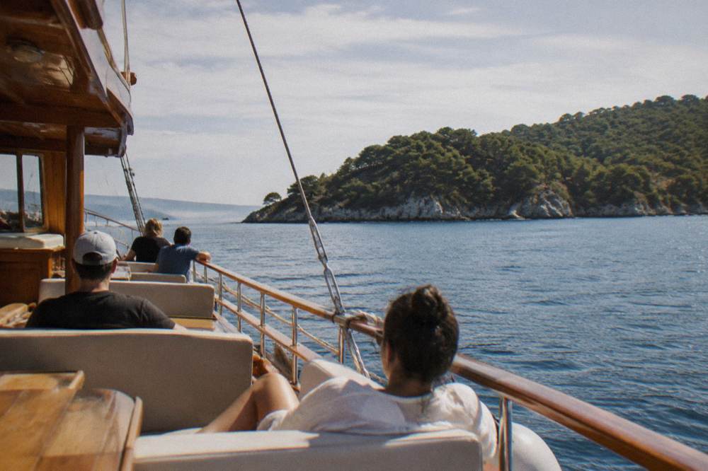 Passengers relaxing on the deck of a wooden cruise boat anchored near a pine covered island