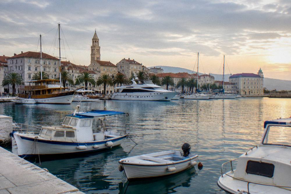 Boats of different sizes moored in a calm harbour at golden hour with stone buildings behind