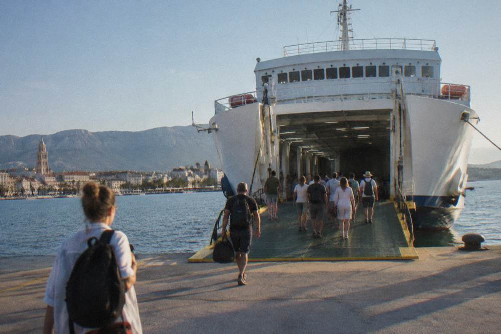 A white car ferry docked at the Split ferry port with passengers boarding on foot