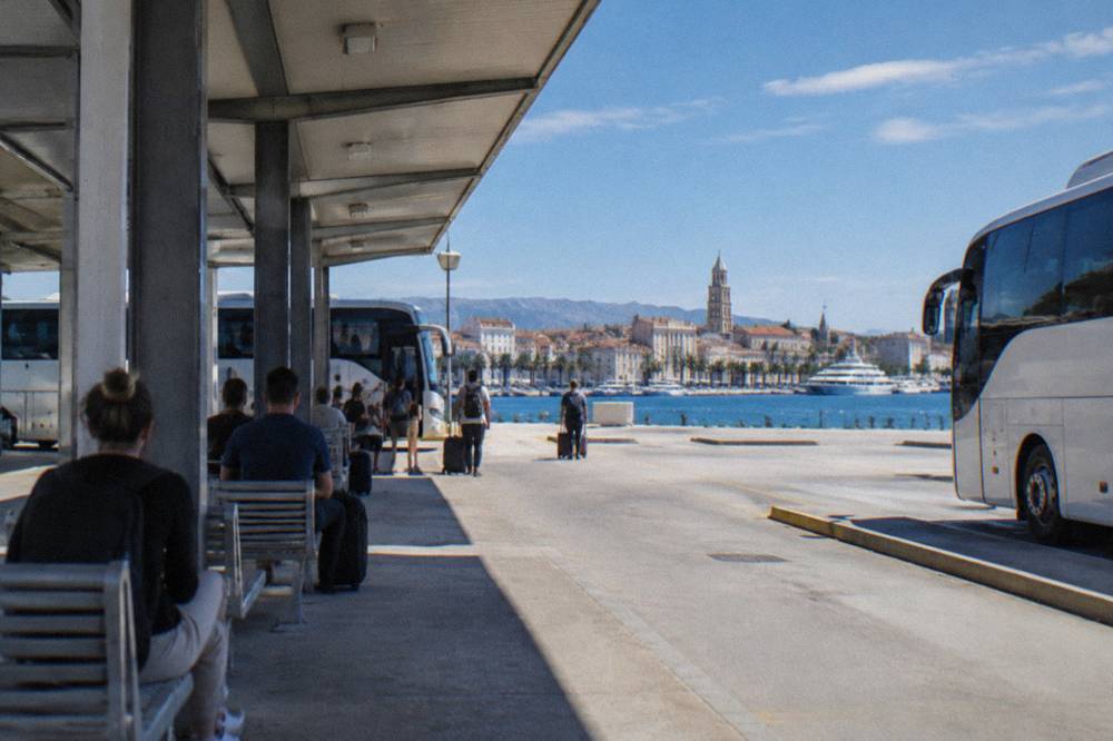 Travellers waiting under the awnings of the Split bus station with the harbour in the background