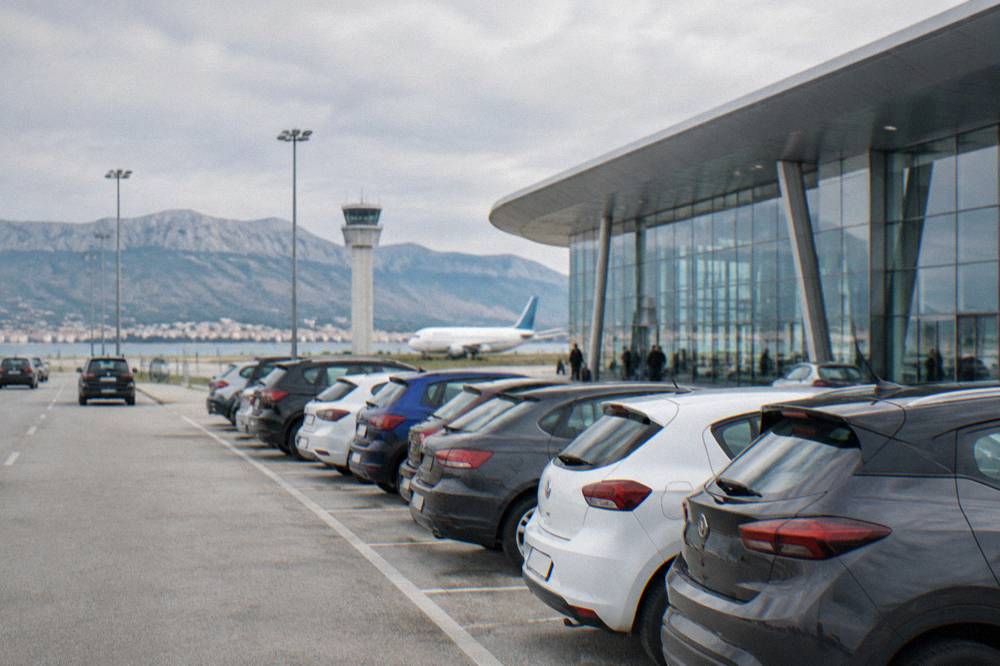 Cars lined up at an airport rental car park beside a modern terminal building