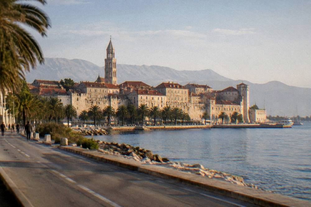 Sunlit walled old town above the sea seen from a coastal road