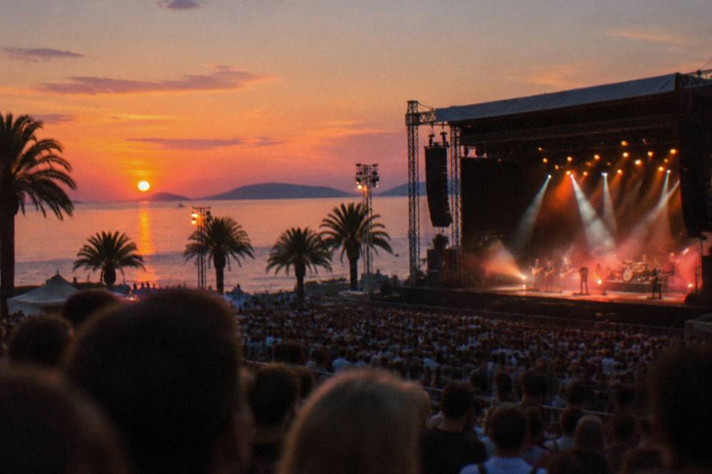 Open air concert stage with crowds and lights at a stadium venue in the evening