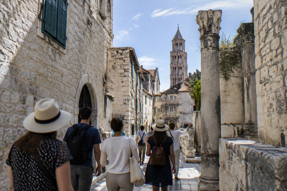 A small group of visitors following a guide through a narrow stone street in an old town