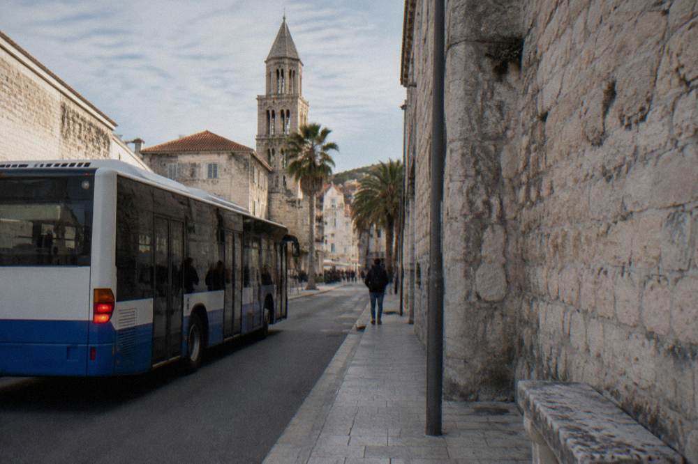 A city bus at a stop near a stone walled old town street