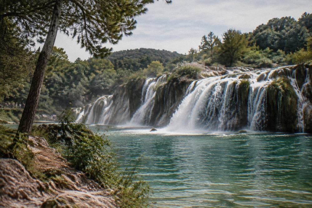 A waterfall pouring over travertine ledges into a green pool in a national park