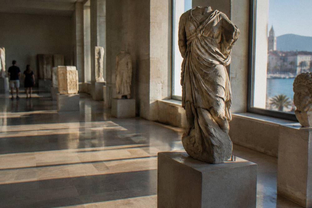 A museum gallery with stone sculpture lit by natural light from tall windows